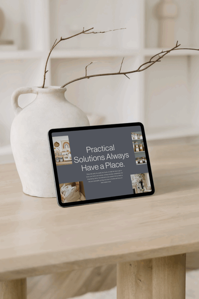A landscape-oriented tablet resting on a light wood table next to a rustic white ceramic vase holding bare decorative branches. The tablet screen displays a dark-themed website interface with the headline "Practical Solutions Always Have a Place." alongside inset images of organized home spaces.