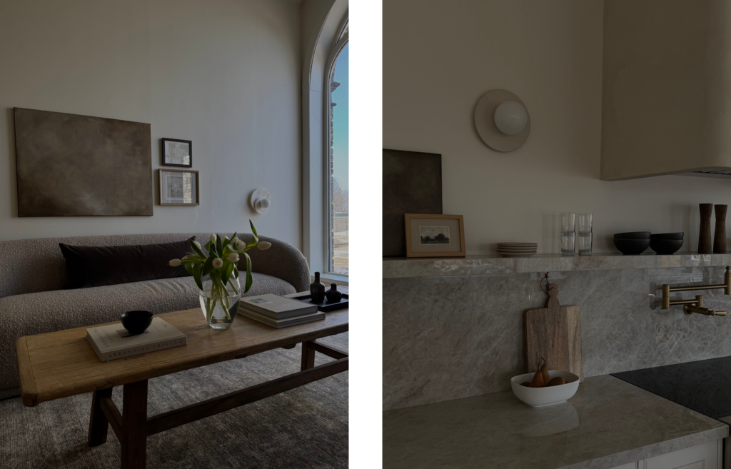 Left side: A minimalist living room with a curved bouclé sofa and a wooden coffee table displaying white tulips in a glass vase and art books. A large, moody, dark brown abstract painting hangs on the white wall above the sofa, next to two smaller framed pieces, near a large arched window.
Right side: A close-up of a modern kitchen counter made of grey-veined marble. A wooden cutting board and a white bowl filled with pears sit on the counter. A marble shelf above holds small ceramic bowls, glasses, and a small framed landscape print resting against the wall beneath a round, minimalist wall sconce.